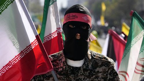 A member of the Iranian paramilitary Basij force holds an Iranian flag as he covers her face in the Palestinian and Lebanese militants style in an annual rally to mark Quds Day, or Jerusalem Day, to support the Palestinians in Tehran, Iran, Friday, April 5, 2024. 