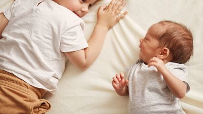 Toddler and baby sibling laying on a bed