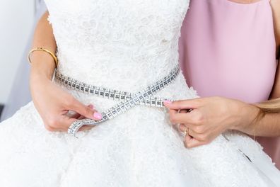 Tailor-woman measuring waist on wedding dress in bridal shop.