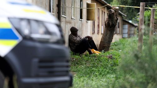 Bir adam, Pretoria yakınlarındaki bir barda meydana gelen kitlesel silahlı saldırıda bulunan kurbanların cesetlerinin bulunduğu yerde oturuyor. (AP Photo/STR)