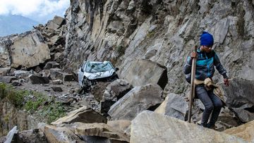 A Nepalese man walks over fallen rocks and past a crushed car on the way to Dhunche. (AAP)