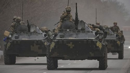 Ukrainian servicemen sit atop armored personnel carriers driving on a road in the Donetsk region.