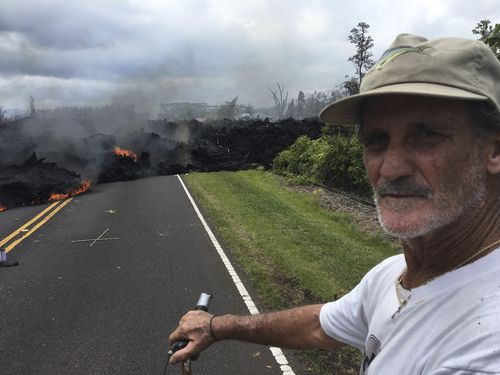 Resident Sam Knox, 65, rides his bicycle to the edge of the road as lava burns across the road. (AAP)