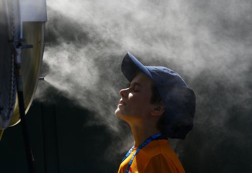 A ball boy cools off in mist sprayed by a water misting fan on a hot summer day at the Australian Open. (AAP)