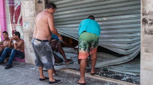 A shopkeeper finds a security door damage in looting after Vitoria police went on strike. (Photo: AFP)