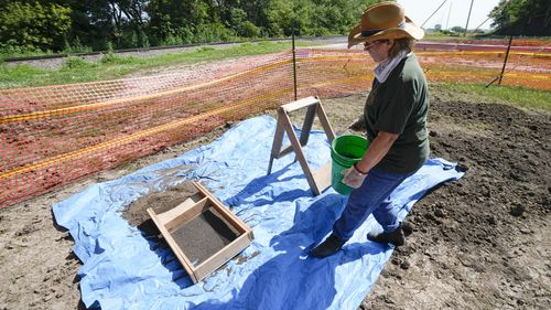 Volunteer Nancy Carlson carries a pail of dirt to be sifted through as workers dig for the suspected remains of children who once attended the Genoa Indian Industrial School.