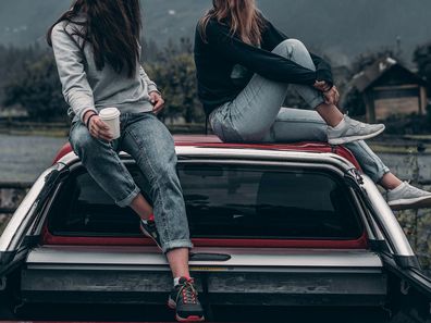 Stock photo of two women sitting on a car.