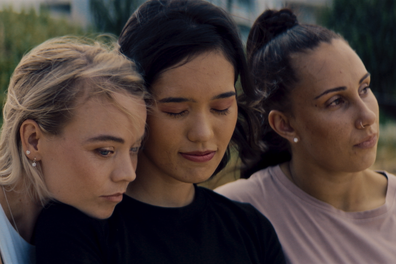 Jane Larkin as Annie, Mei Ichinose as Yui, and Lily Riley as Sylvia share an embrace in The Edge.