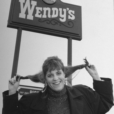 Wendy Morse, daughter of Wendy's fast-food chain founder Dave Thomas, holding up her hair in simulated pigtails under a Wendy's sign