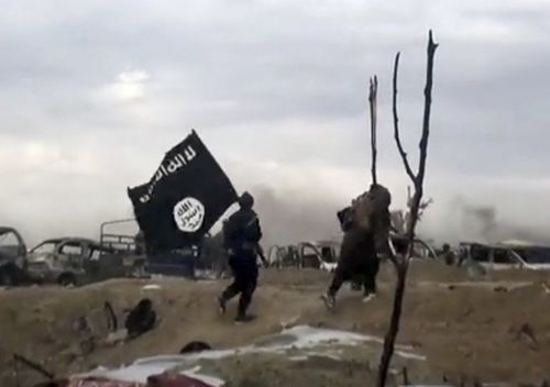 IS fighters walk as they hold the group's flag inside Baghouz in Syria. 