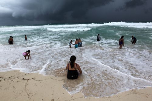 People swim in the turbulent sea at a beach in Cancun as Hurricane Michael descends.