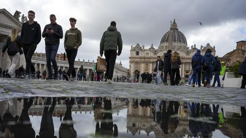 People walk in St. Peter's Square at The Vatican, Friday, Feb. 14, 2025, hours after Pope Francis was hospitalized to undergo some necessary diagnostic tests and to continue his ongoing treatment for bronchitis. (AP Photo/Alessandra Tarantino)