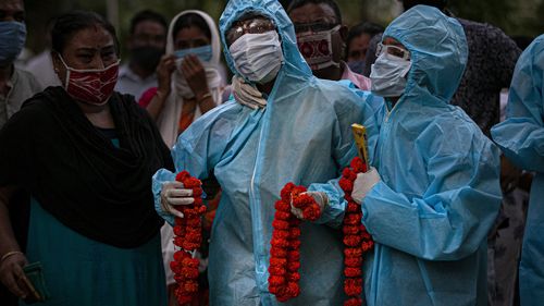 Relatives assist an Indian woman in personal protective equipment offer marigold garlands on the body of her husband  who died of COVID-19 in Gauhati, India, 