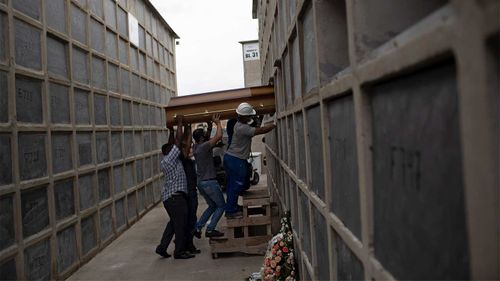 The coffin containing the remains a woman who died from complications related to COVID-19 is placed into a niche by cemetery workers and relatives at the Inahuma cemetery in Rio de Janeiro, Brazil.