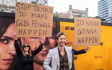 Glen Powell&#x27;s parents hold up signs behind him as they attend the special screening of Hitman in Austin, Texas on May 15.