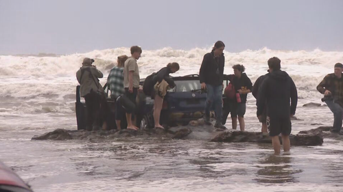 Campers salvage their belongings from a car that washed up on the beach after yesterday's flood.