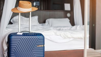 Blue Luggage with hat in modern hotel room after door opening. Time to travel, service, journey, trip, summer holiday and vacation and staycation concepts