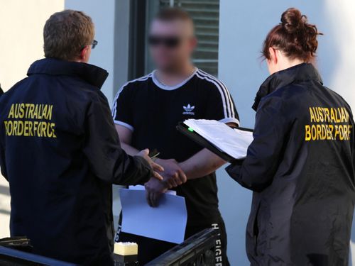 The suspect talks with law enforcement outside his Bathurst home, before he was taken to a local police station over alleged drug and firearm importation offences.