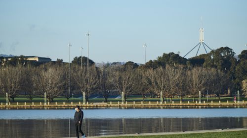A walker wearing a mask beside Lake Burley Griffin in Canberra.