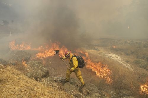 Don Jones, center, a firefighter with Cal Fire Mendocino Unit works with a rake as a wildfire reaches a road. Picture: AAP