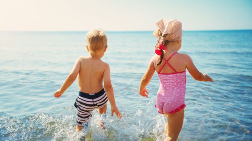 Boy and girl playing on the beach on summer holidays. Children in nature with beautiful sea, sand and blue sky. Happy kids on vacations at seaside running in the water