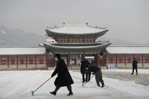 People wearing face masks clear snow at the Gyeongbok Palace, one of South Korea's well-known landmarks, in Seoul, South Korea, Wednesday, Jan. 13, 2021.