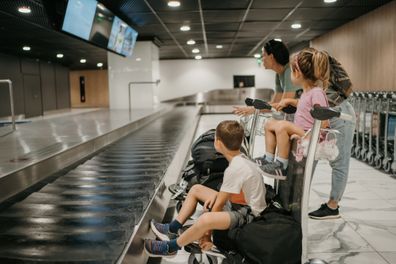 Little brother and sister sitting on luggage cart and waiting for the flight with their mother in airport departure area