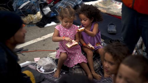 Two little girls who are part of a migrant caravan share a sandwich in Tijuana, Mexico.