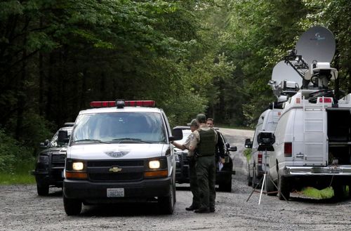 Washington State Fish and Wildlife Police confer with an individual from the King County Medical Examiner's office on a remote gravel road above Snoqualmie, Wash., following a fatal cougar attack, Saturday, May 19, 2018. One man was killed and another seriously injured when they encountered a cougar Saturday while mountain biking in Washington state, officials said. (Alan Berner/The Seattle Times via AP) 