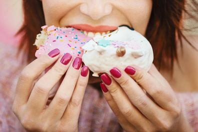 Unrecognizable young woman eating donuts at city street.