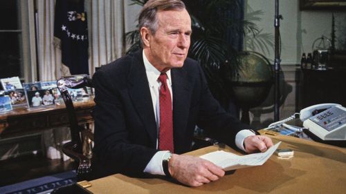 George H.W. Bush poses for photographers after delivering an address to the nation from the Oval Office of the White House in Washington, DC on Christmas Day, December 25, 1991 announcing the resignation of President Mikhail Gorbachev as President of the Union of Soviet Socialist Republics, marking the collapse of the Soviet Union and the end of the Cold War.