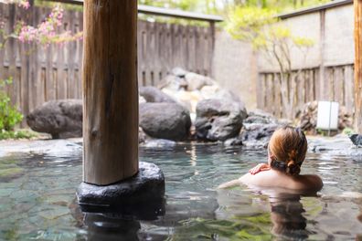 A rear view of a woman relaxing in a Japanese hot spring outdoor bath.