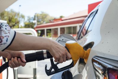 A close up shot of an unrecognisable woman using a fuel pump and filling up a vehicle.