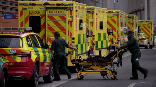 Paramedics push a trolley next to a line of ambulances outside the Royal London Hospital in the Whitechapel area of east London, Thursday, Jan. 6, 2022. 