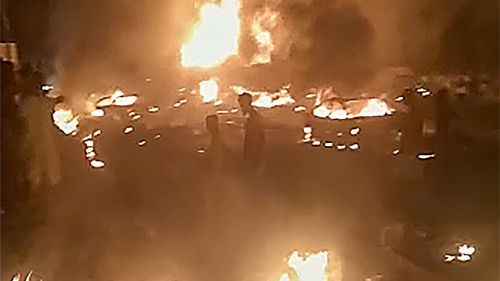 In this image made from video, people walk by burning debris following the explosion of an oil tanker in the Wellington suburb of Sierra Leone's capital Freetown.