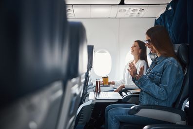 Female on passenger seat of plane clapping her hands with joy and laughing while staring at her laptop display