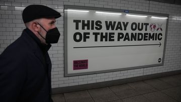 A man wearing a face mask to curb the spread of coronavirus walks past a health campaign poster from the One NGO, in an underpass leading to Westminster underground train station, in London, Thursday, January 27, 2022. 