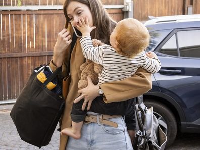 Stock photo of a mum carrying her child and several bags while talking on her mobile phone