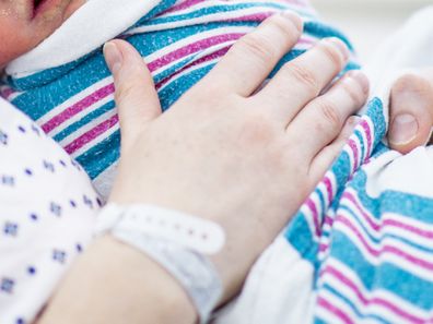 Woman in hospital holding newborn baby to her chest.