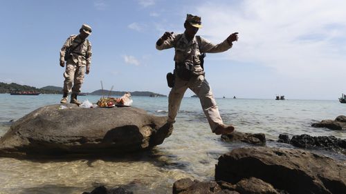 Cambodia soldiers leap rocks after offering prayers in hopes of finding the British national.