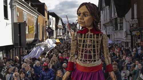 Little Amal processes through Cantebury in England, followed by hundreds of members of the public and school children.