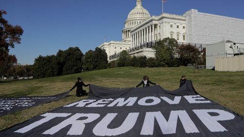 Demonstrators kneel near large banners on the lawn adjacent to the US Capitol.