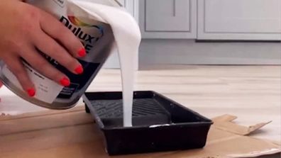 Woman pours white paint into a paint tray.