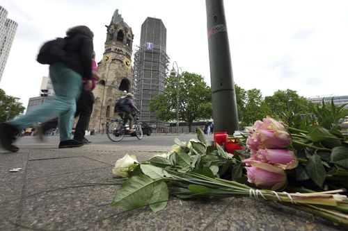 People walk past flowers and candles at the Kaiser Wilhelm Memorial Church in Berlin, Germany, Thursday, June 9, 2022. 