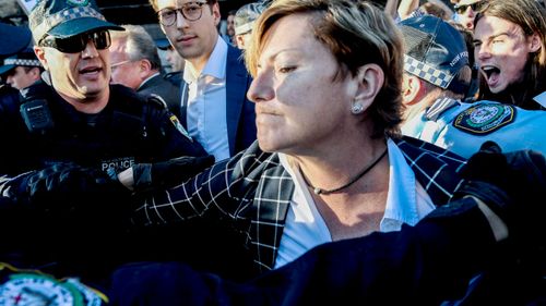 Police rush to the assistance of Christine Forster as she's caught up in protests at an event for her brother, former prime minister Tony Abbott, in Redfern, Sydney. (AAP)