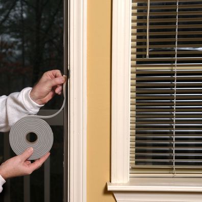 Homeowner applying weather stripping to stop air leaks around a doorway