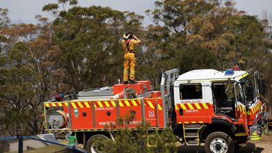NSW Rural Fire Service crews watch on as water bombing helicopters fight a fire burning in bushland at Penrose in the NSW Southern Highlands, 165km south of Sydney, Friday, January 10, 2020. 