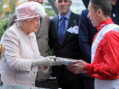 Queen Elizabeth II presents jockey Frankie Dettori with his prize for winning the Queen Elizabeth II Stakes at Ascot Racecourse on October 21, 2017.
