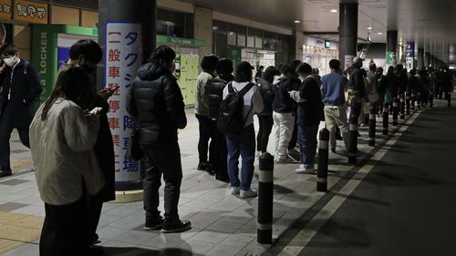 Люди выстраиваются в очередь, чтобы дождаться такси в Сендае, префектура Мияги, северная Япония, рано утром в четверг, 17 марта 2022 года, после землетрясения.