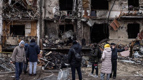 People look at a damaged residential block hit by an early morning missile strike  in Kyiv.